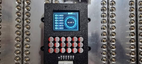 Close-up of a Heltec 5.5a 6s Balancer and display with a digital screen showing voltage readings, surrounded by symmetrical rows of metallic circular connectors.