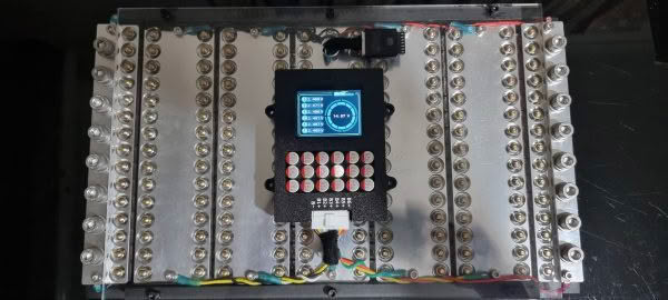 A close-up of the Heltec 5.5a 6s Balancer and display shows its metallic grid components centered with a digital screen and buttons. Colorful wires connect around the edges, while a USB drive is inserted at the top.