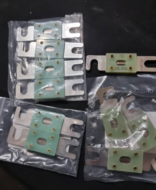 Five sets of CNL Fibre Glass Fuses with green labels and gold contacts are displayed in transparent plastic bags on a dark surface.