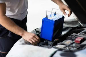 Person installing blue car battery under hood.